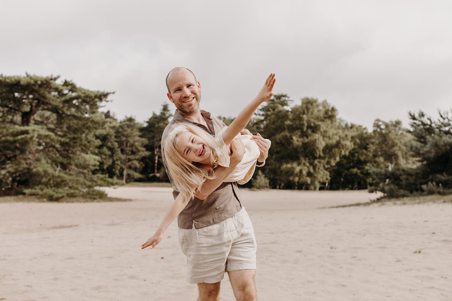 Vader stoeit met kinderen tijdens gezinsfotoshoot in de duinen in Huizen