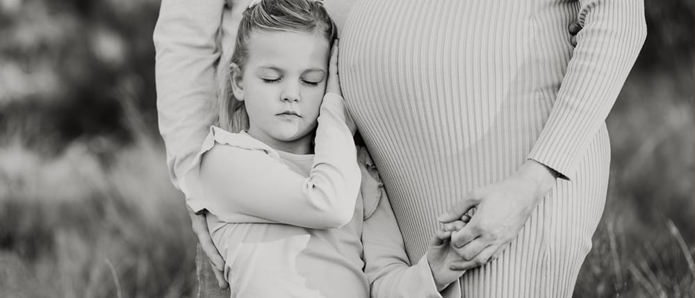 Zwartwit foto van meisje die knuffelt met zwangere buik van moeder tijdens een zwangerschapsshoot